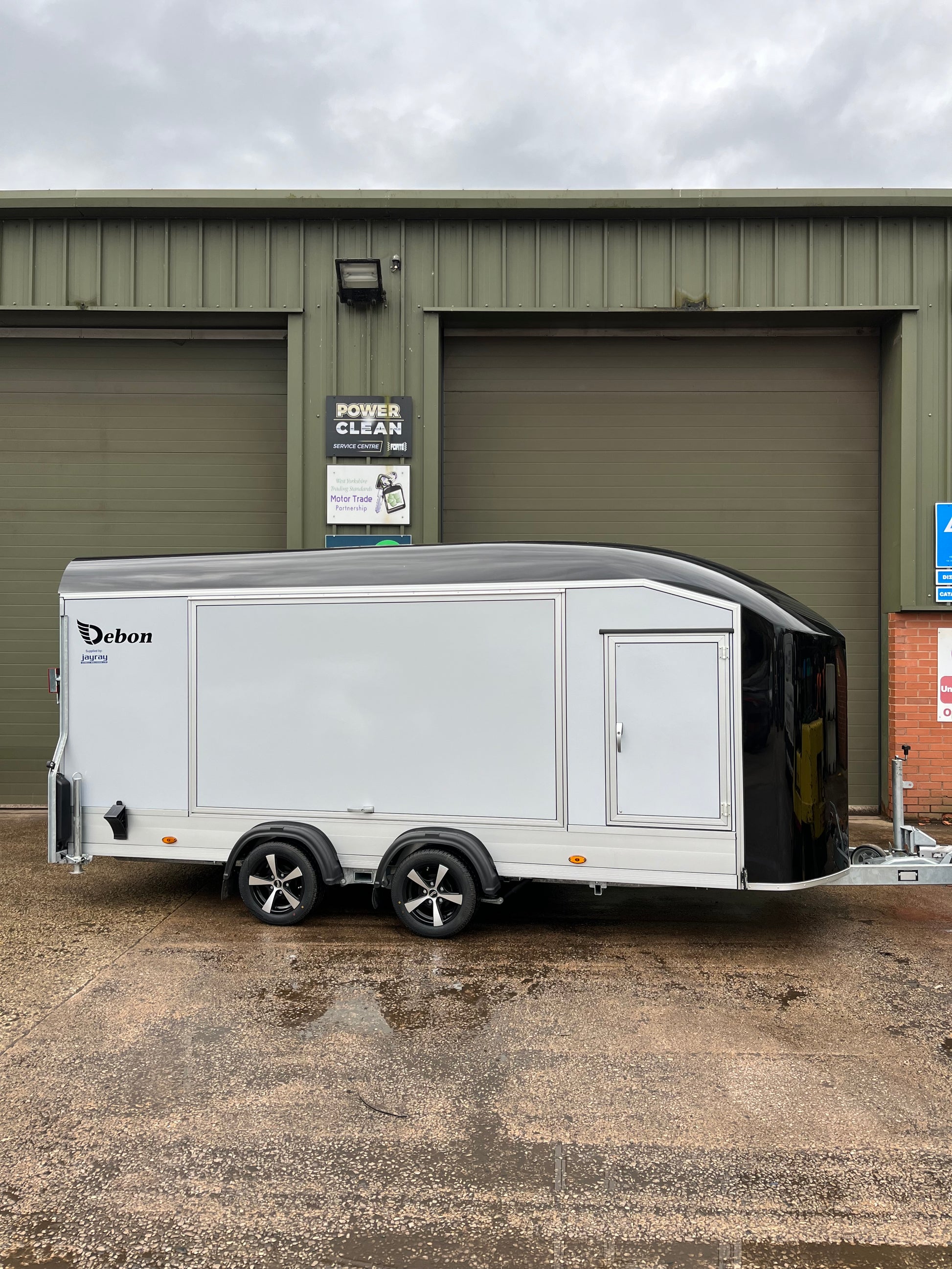 A white and black Debon C1000 box trailer car transporter with Gullwing doors, LED loading lamps, and an automatic jockey wheel, side view